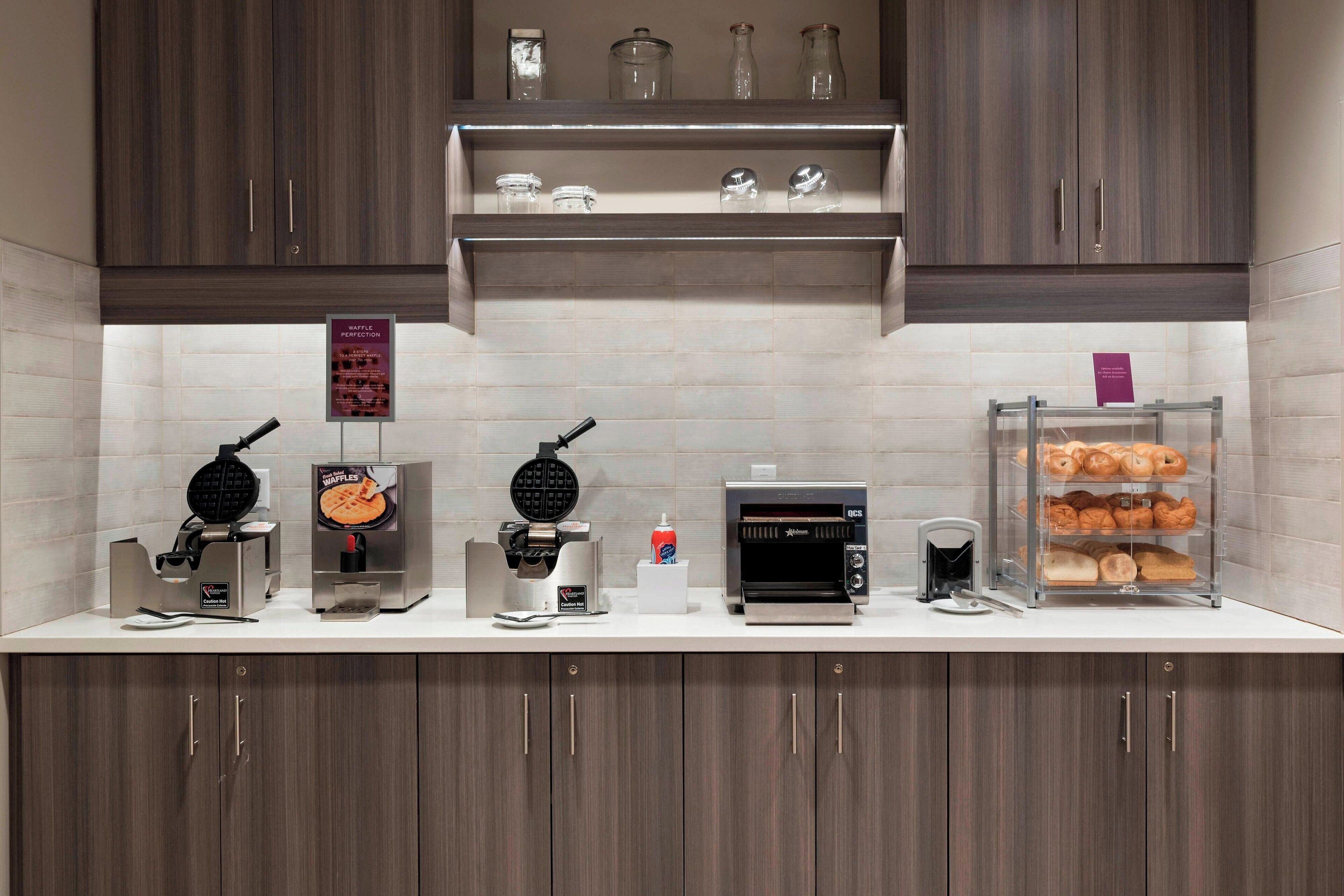 A kitchen with waffle makers, a toaster, and a display case with pastries.
