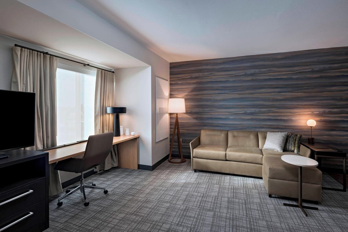 Une chambre d’hôtel équipée d’un bureau, d’une chaise, d’un canapé, d’une télévision, d’une lampe et d’un mur au décor texturé.