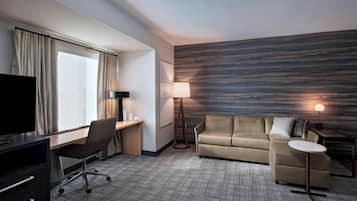 Habitación de hotel con escritorio, silla, sofá, televisión, lámpara y pared con diseño texturizado.