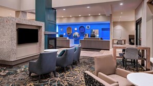 Un vestíbulo de hotel con mostrador de recepción, zona de estar y televisor montado en la pared.