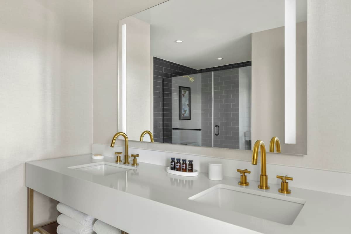 Un baño moderno con dos lavamanos, grifos dorados y un espejo grande.