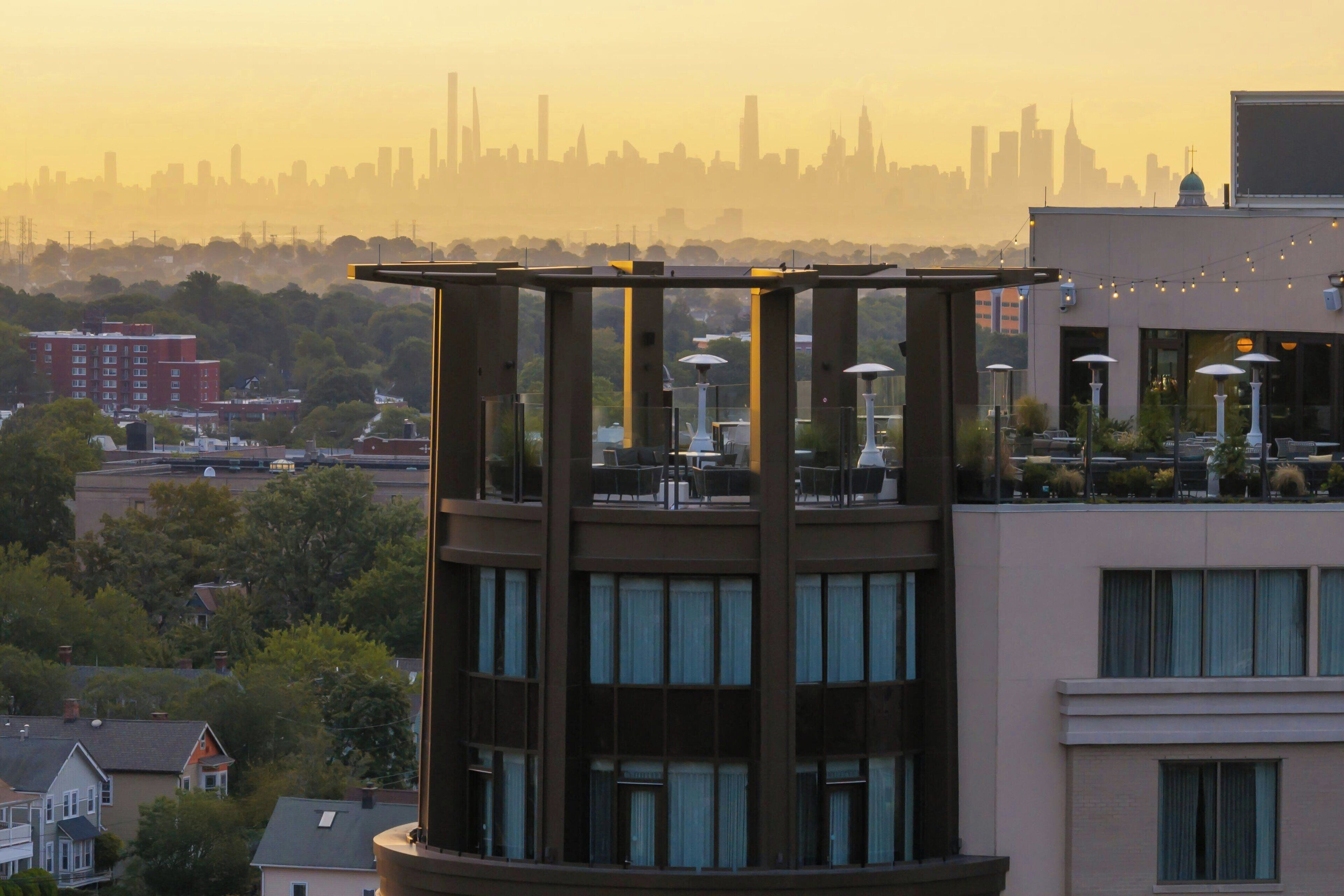 A multi-story building with a rooftop terrace featuring outdoor seating and string lights.