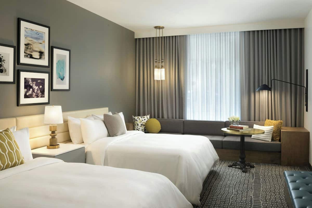 Habitación de hotel con dos camas, un sofá, una mesita y una lámpara.