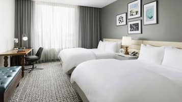 Een hotelkamer met twee bedden, een bureau met stoel, een lamp en ingelijste foto's aan de muur.