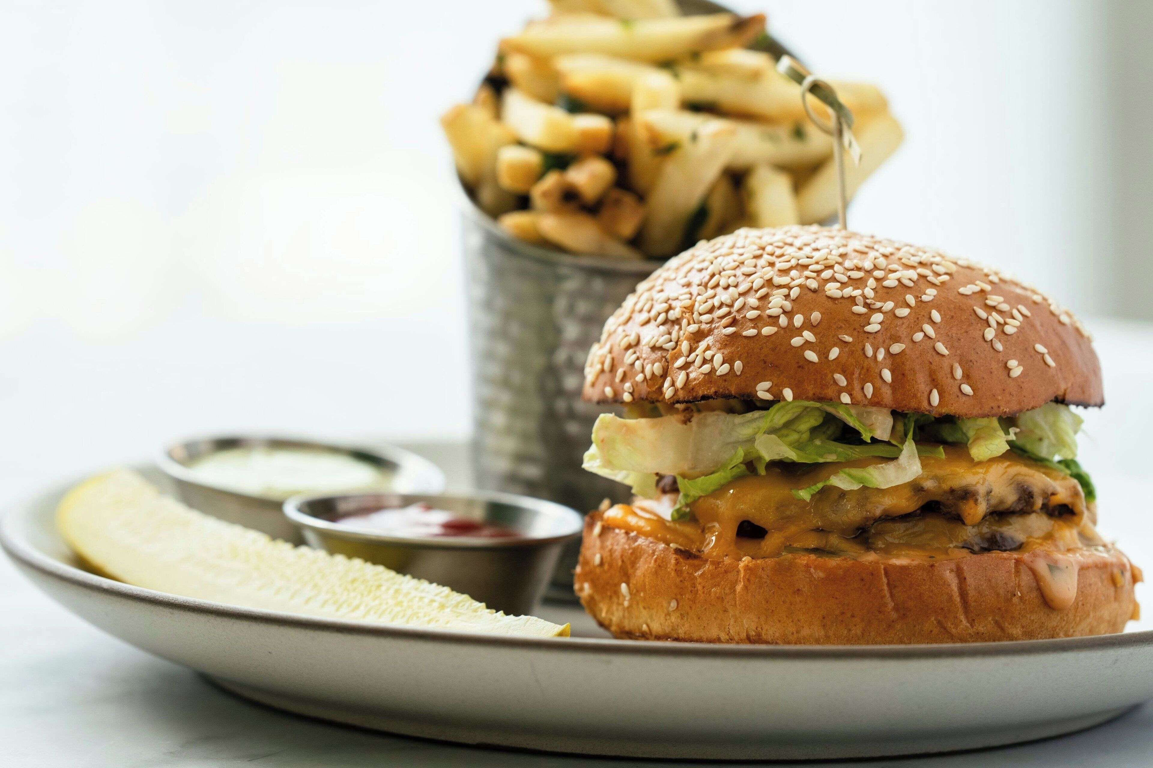Een hamburger met sesamzaadjes op het broodje, vergezeld van friet en een portie saus.