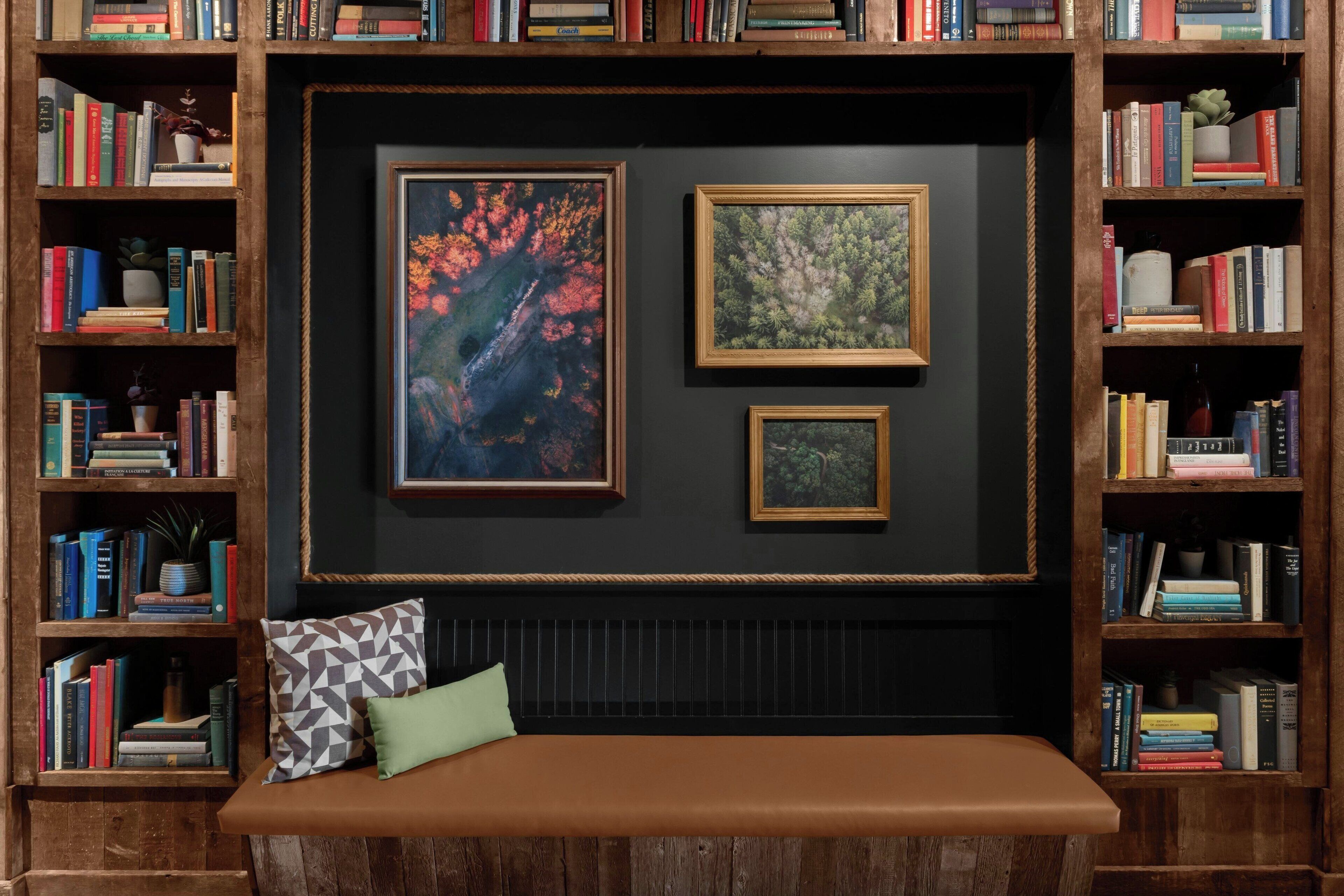A cozy reading nook with a cushioned bench, surrounded by bookshelves filled with books and framed pictures on the wall.
