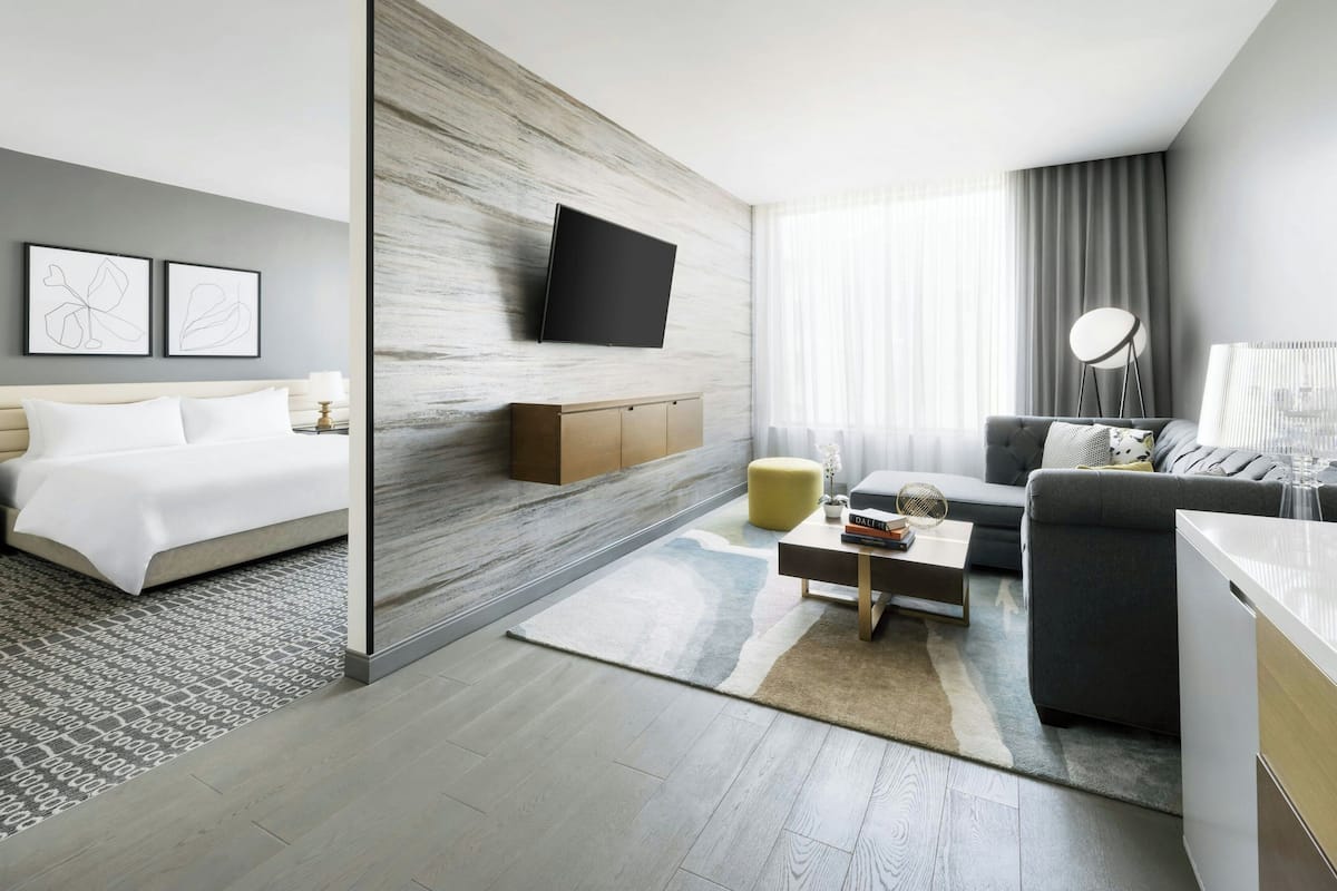 Una habitación de hotel moderna con cama, sofá, mesa de centro y televisor montado en la pared.