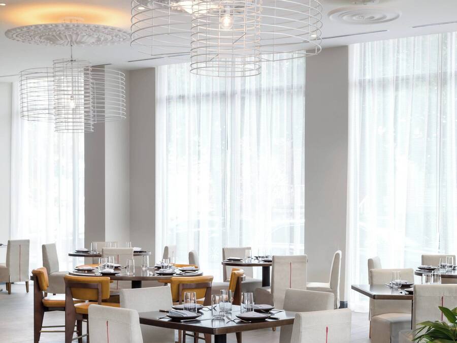 A modern dining area with round tables, white chairs, and decorative ceiling lights.