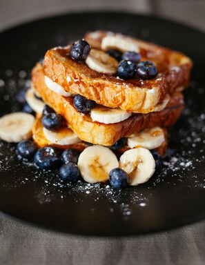A stack of French toast with bananas and blueberries on a black plate.