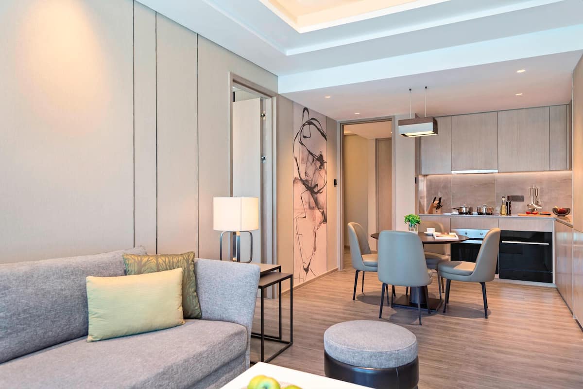 Een moderne woonkamer met een grijze bank, een eettafel met stoelen, en een keuken met houten kasten en een aanrecht.