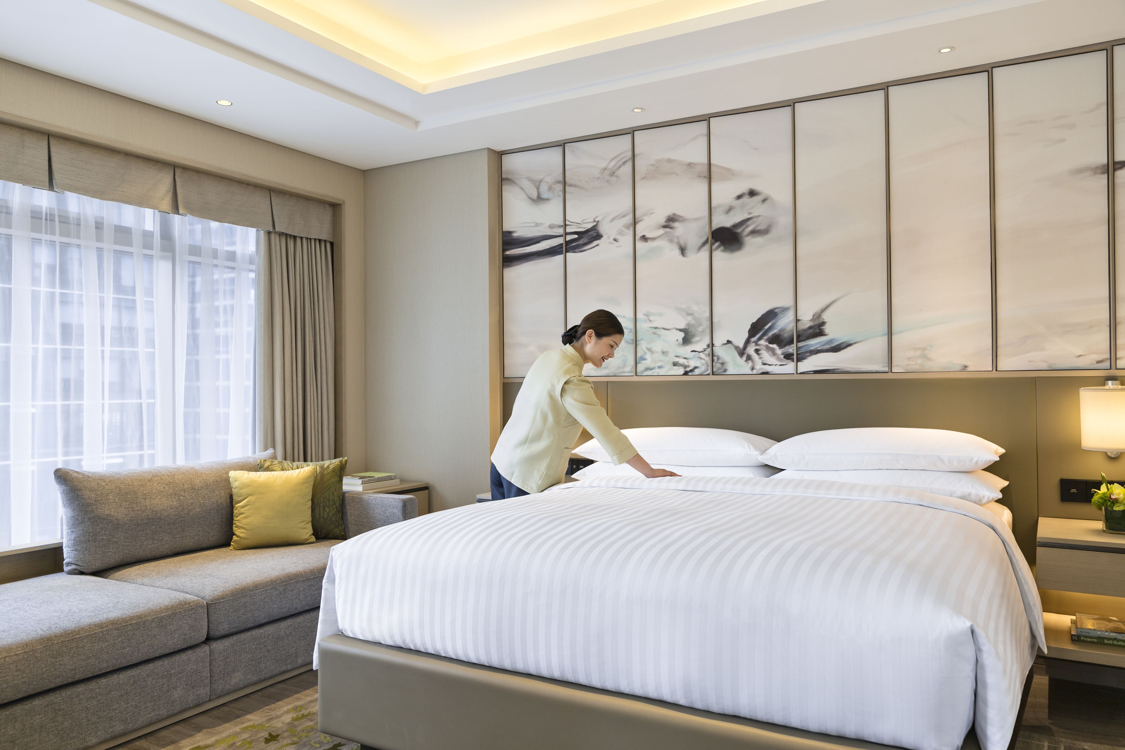 A hotel room with a large bed, a sofa, a nightstand, and a wall with abstract art.