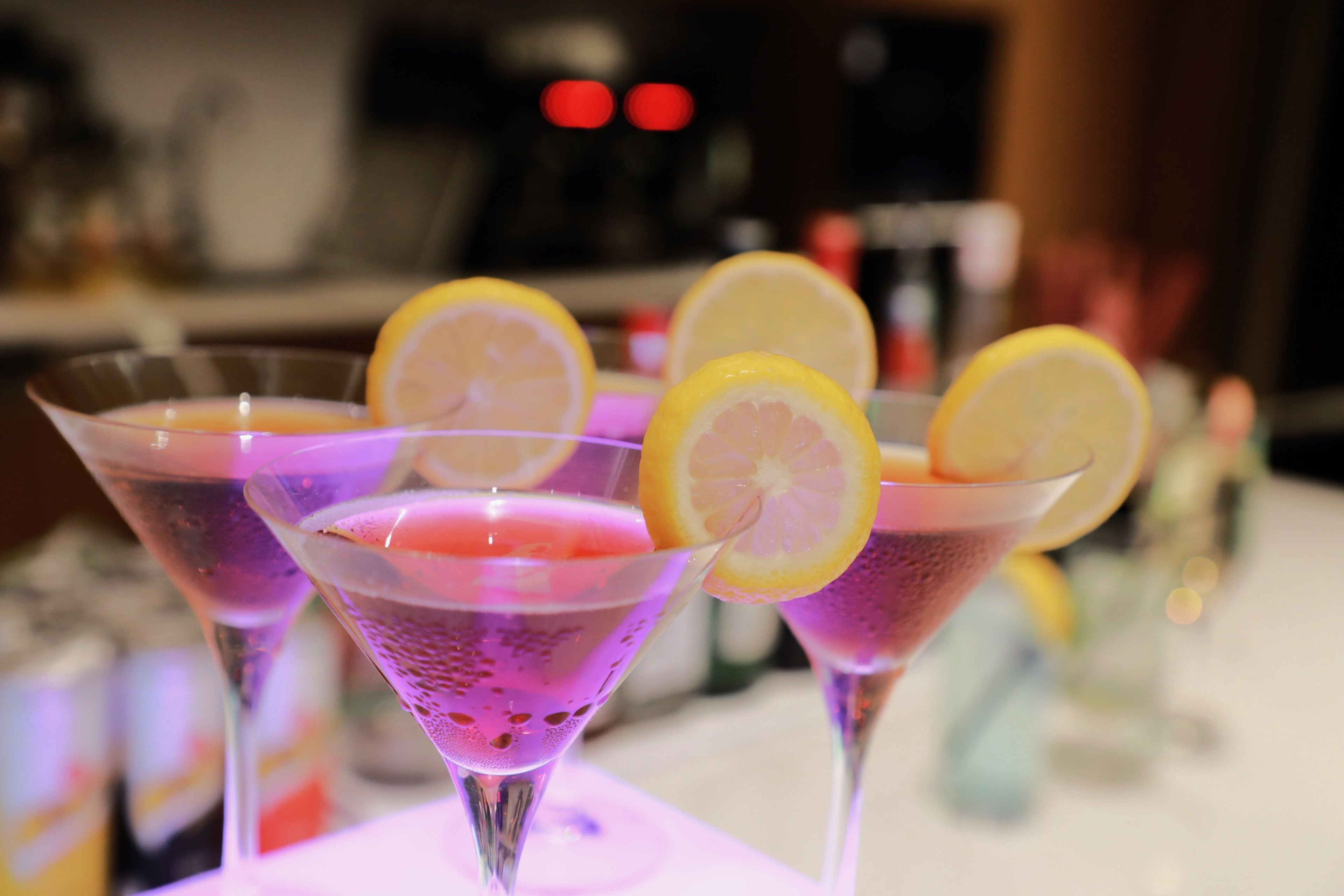 Tre bicchieri da martini con una bevanda viola e fette di limone su un tavolo.
