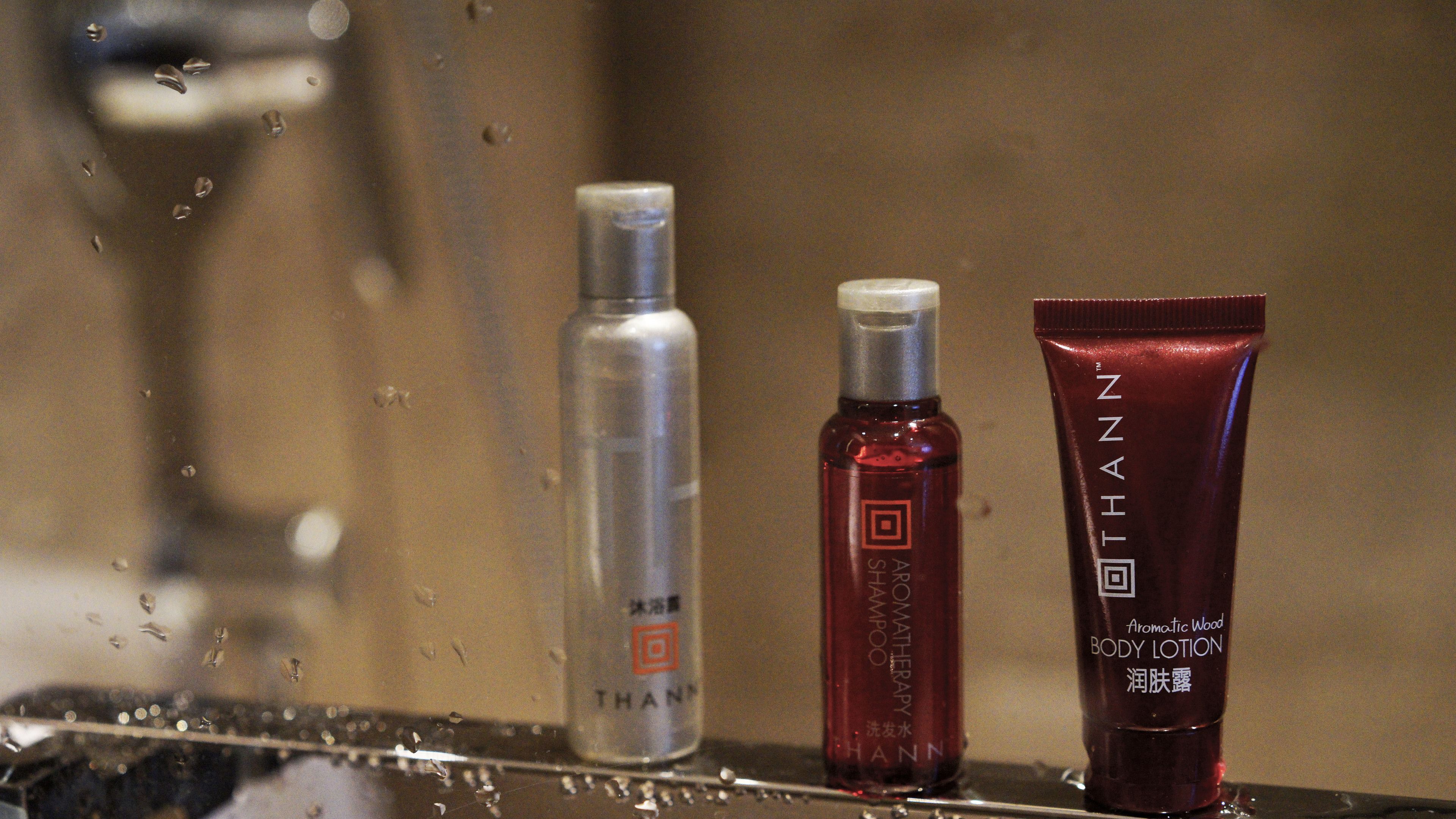 Three bottles of THANN body lotion on a wet surface.
