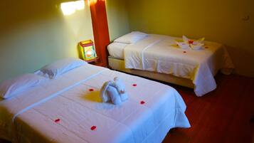 Two single beds with white linens and rose petals, a nightstand with a lamp, and a wall-mounted light fixture.