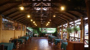 An indoor dining area with wooden tables and chairs, a tiled floor, and a high ceiling with hanging lights. - La Patarashca Hotel (Tarapoto)