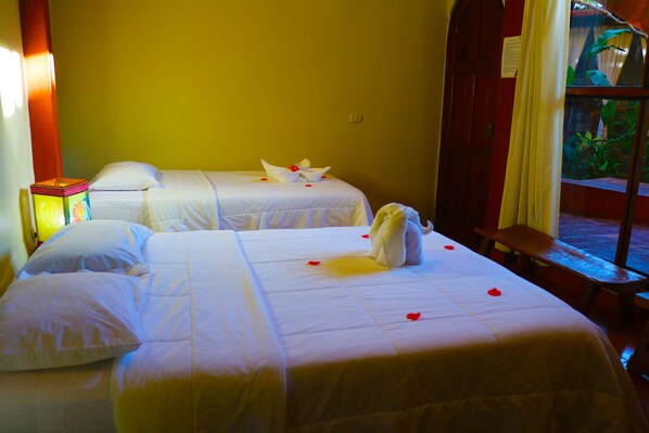 Two single beds with white linens, a bedside table with a lamp, and a window with a view of greenery.