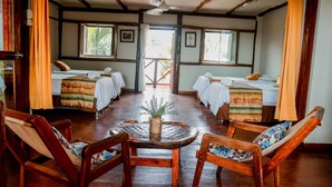 A traditional room with wooden floors, two single beds with striped bedding, a round wooden table with a plant, and a wooden chair with a floral cushion. - La Patarashca Hotel (Tarapoto)