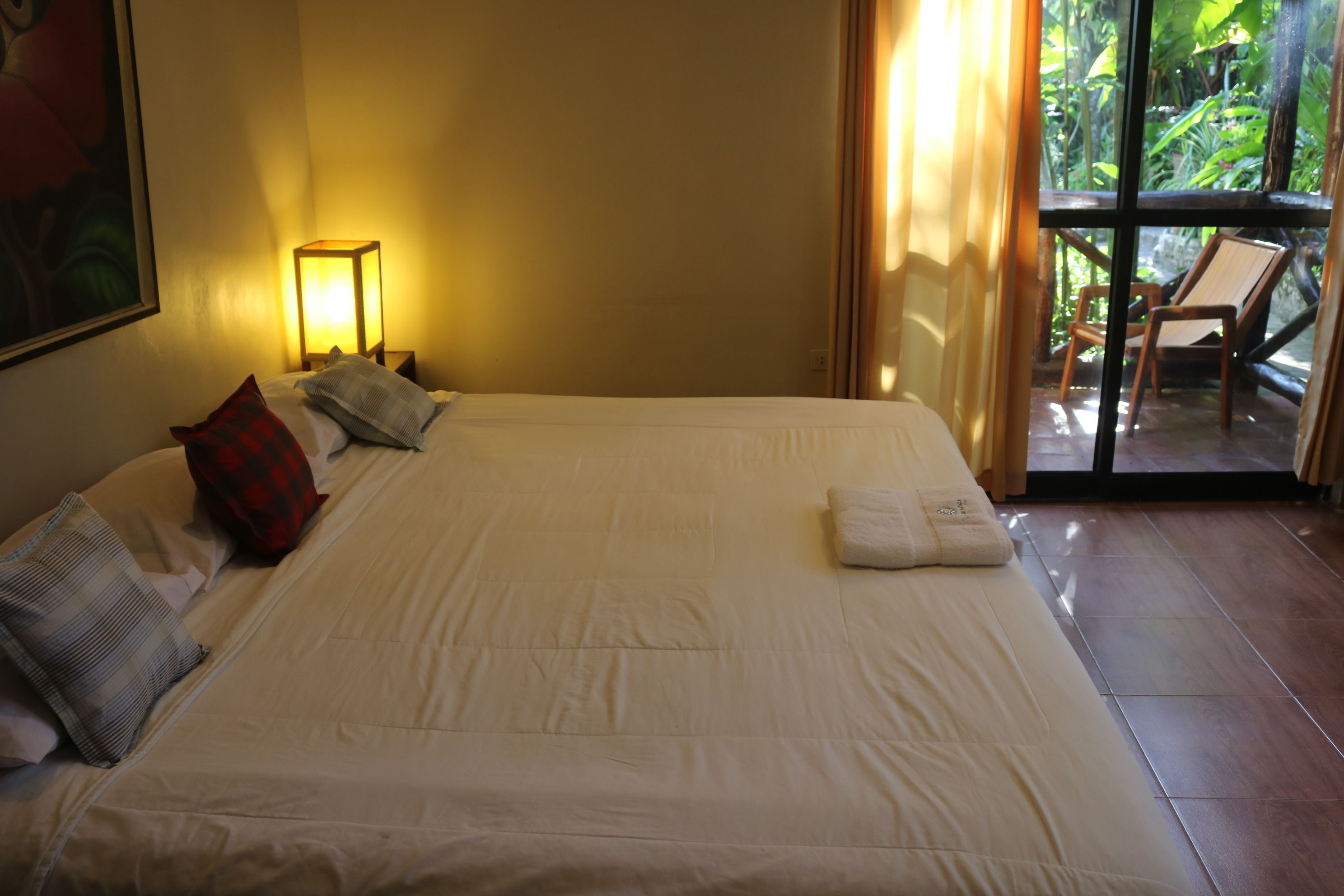 Une chambre d’hôtel avec un grand lit, une table de chevet avec une lampe et une vue sur l’extérieur grâce à une porte vitrée.