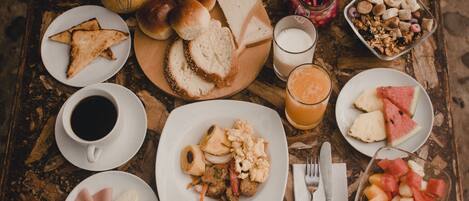 A wooden table with various breakfast items including bread, pastries, fruit, and beverages.