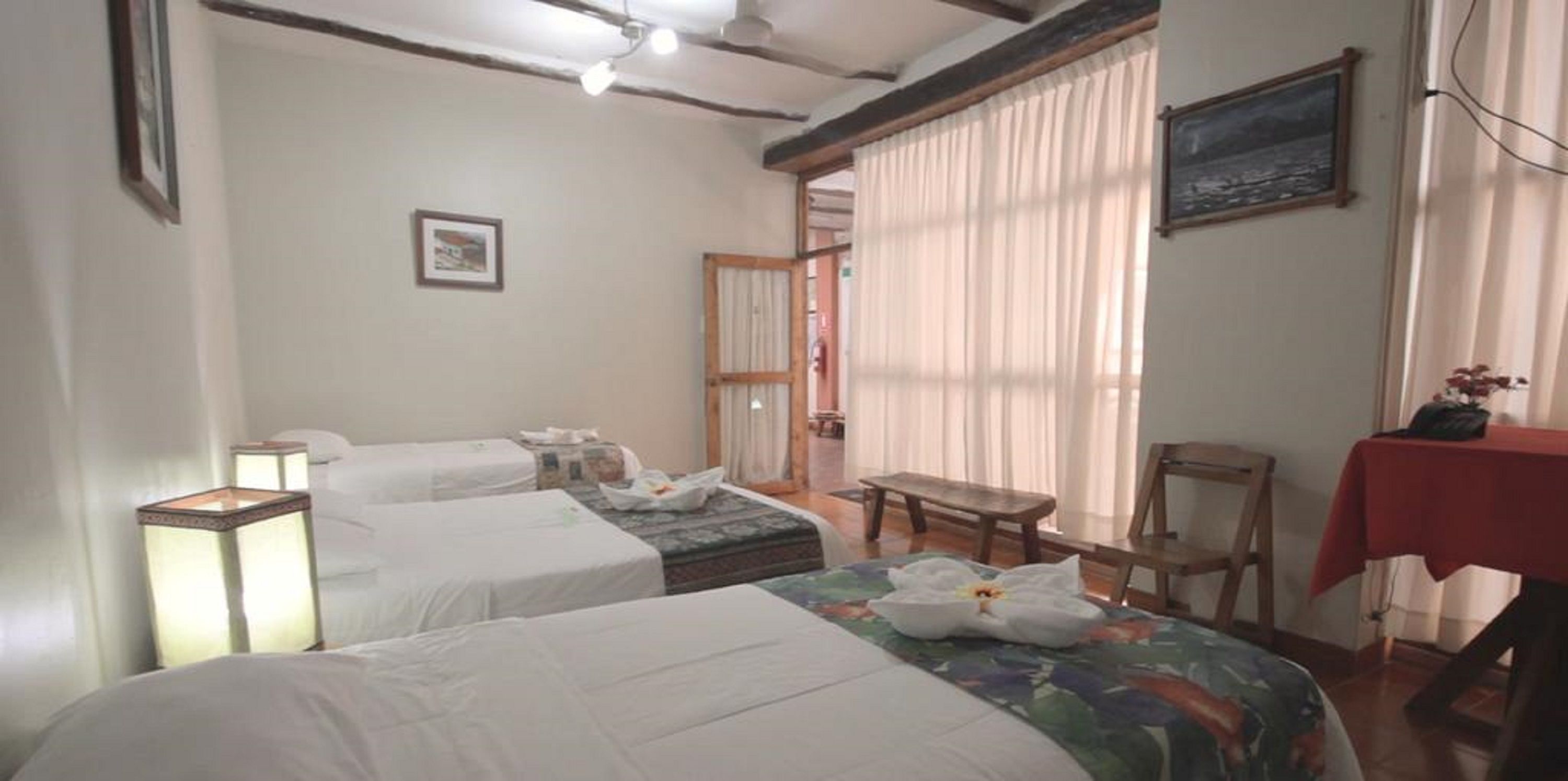 Habitación de hotel con dos camas, una mesita, una silla, un escritorio y una ventana con cortinas.