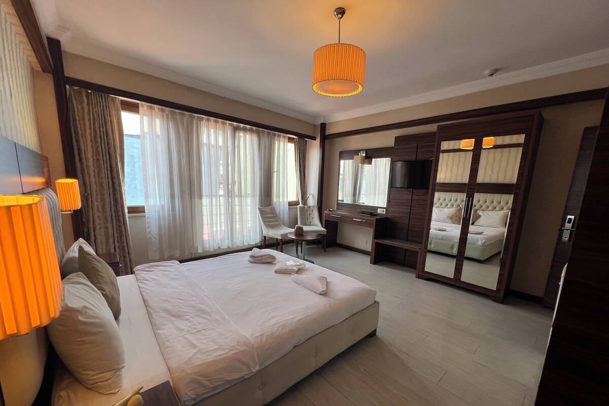 A hotel room with a large bed, a desk with a chair, a wardrobe, and a TV.