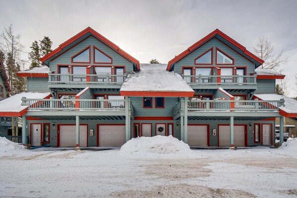 Une grande maison à plusieurs étages, dotée d’une architecture symétrique, avec deux balcons à chaque étage, plusieurs portes de garage et un paysage enneigé.