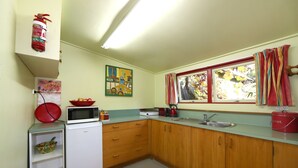 A compact kitchen with a microwave, sink, and a small refrigerator. There is a window with curtains and a fire extinguisher mounted on the wall.