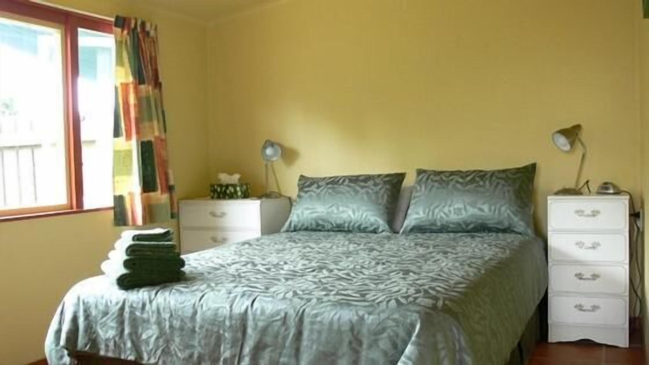 Ein Schlafzimmer mit einem Bett, zwei Nachttischen, einer Lampe, einer Kommode und einem Fenster mit Vorhängen.