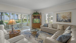 A spacious living room with a beige sofa, a glass coffee table, and a view of the ocean through large windows. - Island House Beach Resort 10S (Siesta Key)