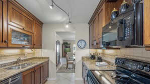 A kitchen with wooden cabinets, granite countertops, a stainless steel sink, a black stove, and a microwave. - Island House Beach Resort 10S (Siesta Key)