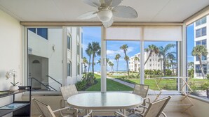 A room with a glass table and chairs, a ceiling fan, and a view of palm trees and buildings. - Island House Beach Resort 10S (Siesta Key)