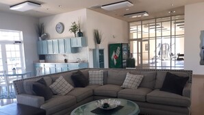 Ein modernes Wohnzimmer mit einem Ecksofa, einem Glastisch und einer Küchenzeile mit hellblauen Schränken.