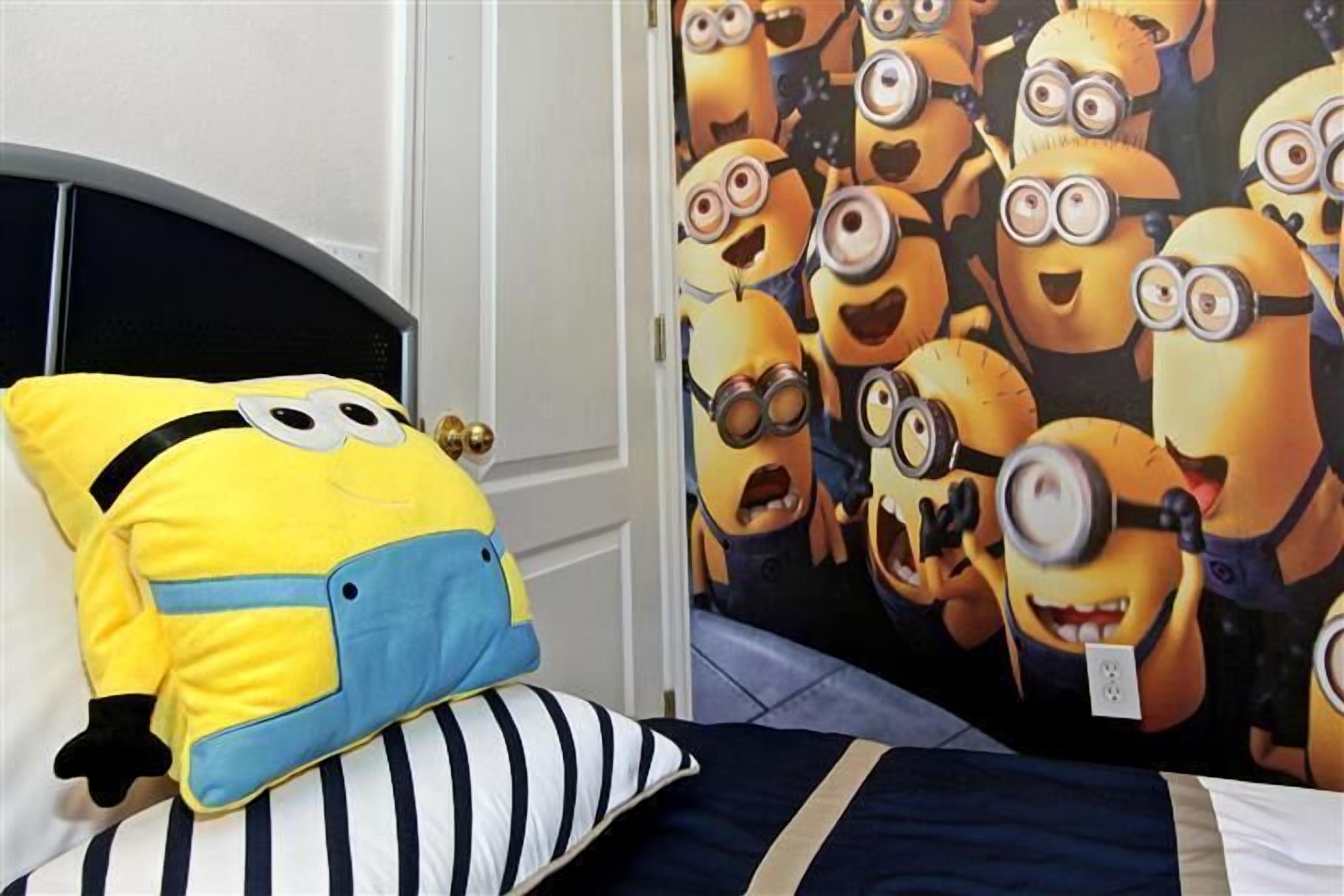 A bedroom with a bed, a pillow, and a wall with a Minion-themed wallpaper.