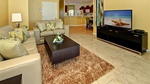 Ein Wohnzimmer mit einer Couch, einem Couchtisch, einem Fernseher und einer Küche im Hintergrund.