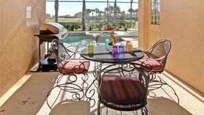 Eine Terrasse mit Grill, Tisch und Stühlen sowie Blick auf Pool und Palmen.