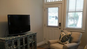 A living room with a television on a cabinet, a door with starfish decorations, and a window with blinds. - Seabrook - On Turtle Time (Pacific Beach)