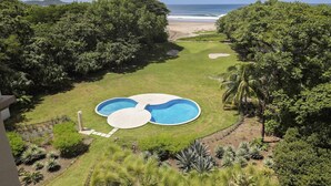 Une piscine de forme circulaire, entourée d’une végétation luxuriante et offrant une vue sur la plage.