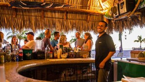 Un espace bar doté d’un toit de chaume, d’un barman et offrant une vue sur l’océan.