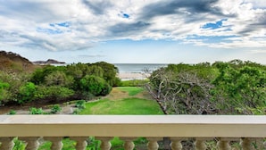 Une vue sur la côte, prise depuis un balcon, avec une zone herbeuse, des arbres et une plage en arrière-plan.