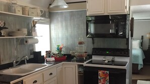 A compact kitchen with white cabinets, a black oven, and a microwave. - Tiny house with full-size amenities tucked away in the countryside (Sulphur)