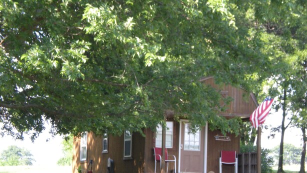 A two-story house with a porch, a flag, and a well-maintained lawn. - Tiny house with full-size amenities tucked away in the countryside (Sulphur)