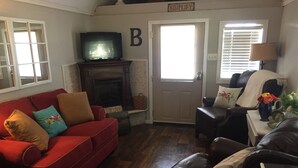 A living room with a red sofa, a black leather chair, a fireplace, and a door with a 'B' sign. - Tiny house with full-size amenities tucked away in the countryside (Sulphur)