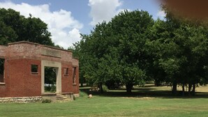 A brick building with a large tree in the background. - Tiny house with full-size amenities tucked away in the countryside (Sulphur)