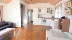 Ett modernt kök med vita skåp, en bänkskiva i trä och en inbyggd ugn. Det finns en matplats med ett vitt bord och stolar, och ett vardagsrum med en soffa och ett soffbord.