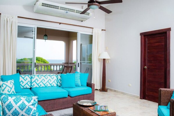 A balcony with a sofa, a lamp, and a door. - Río Dulce V-13: Oceanview Penthouse (Hacienda Iguana)