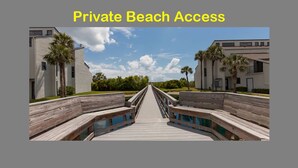 Een houten looppad dat leidt naar een privéstrand met moderne gebouwen aan weerszijden.