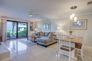 Un salon spacieux avec un grand canapé, une table à manger avec des chaises et une porte-fenêtre coulissante donnant sur un balcon.