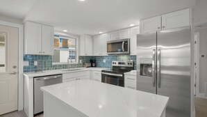 A modern kitchen with white cabinetry, a stainless steel refrigerator, a microwave, and a dishwasher.
