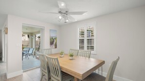 A dining area with a wooden table and chairs, a ceiling fan, and a window with shutters.