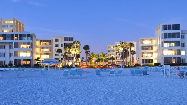 A beach with rows of sun loungers and a hotel in the background.